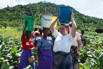 Marthe fra sentralstyret på en åker i Malawi sammen med Malawiske bønder. Alle holder hver sin bøtte på hodet. 
