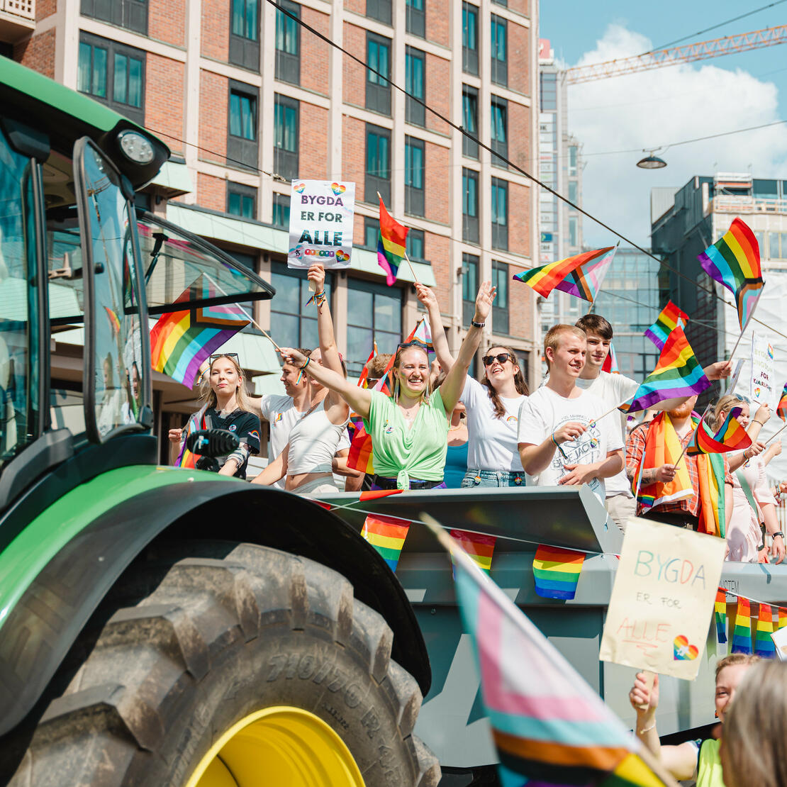 Oslo Pride 2023. Mange folk med regnbueflagg og plakater som står på en henger bak traktor i paraden.