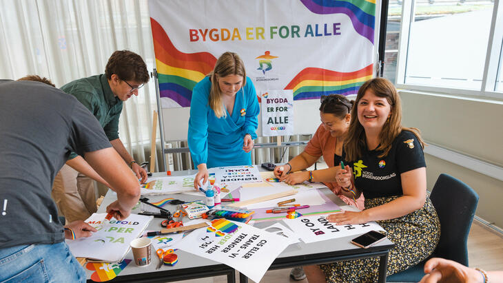 Plakatverksted før Oslo Pride. Flere BU-ere rundt et rotete bor fylt med plakater, tusjer og lim