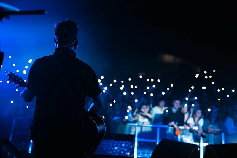 Bilde av en artist på scenen og publikum med lys på telefonen under en konsert. 